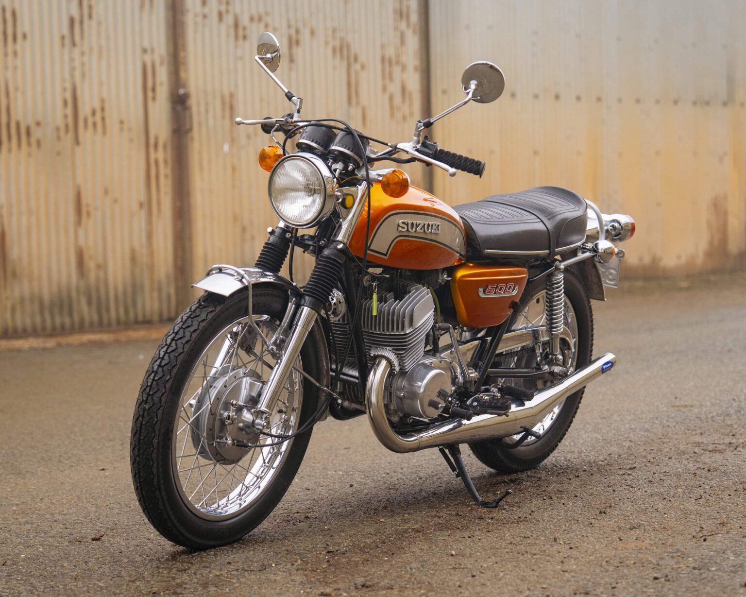 Vintage Suzuki motorcycle parked outdoors with a wooden fence background.