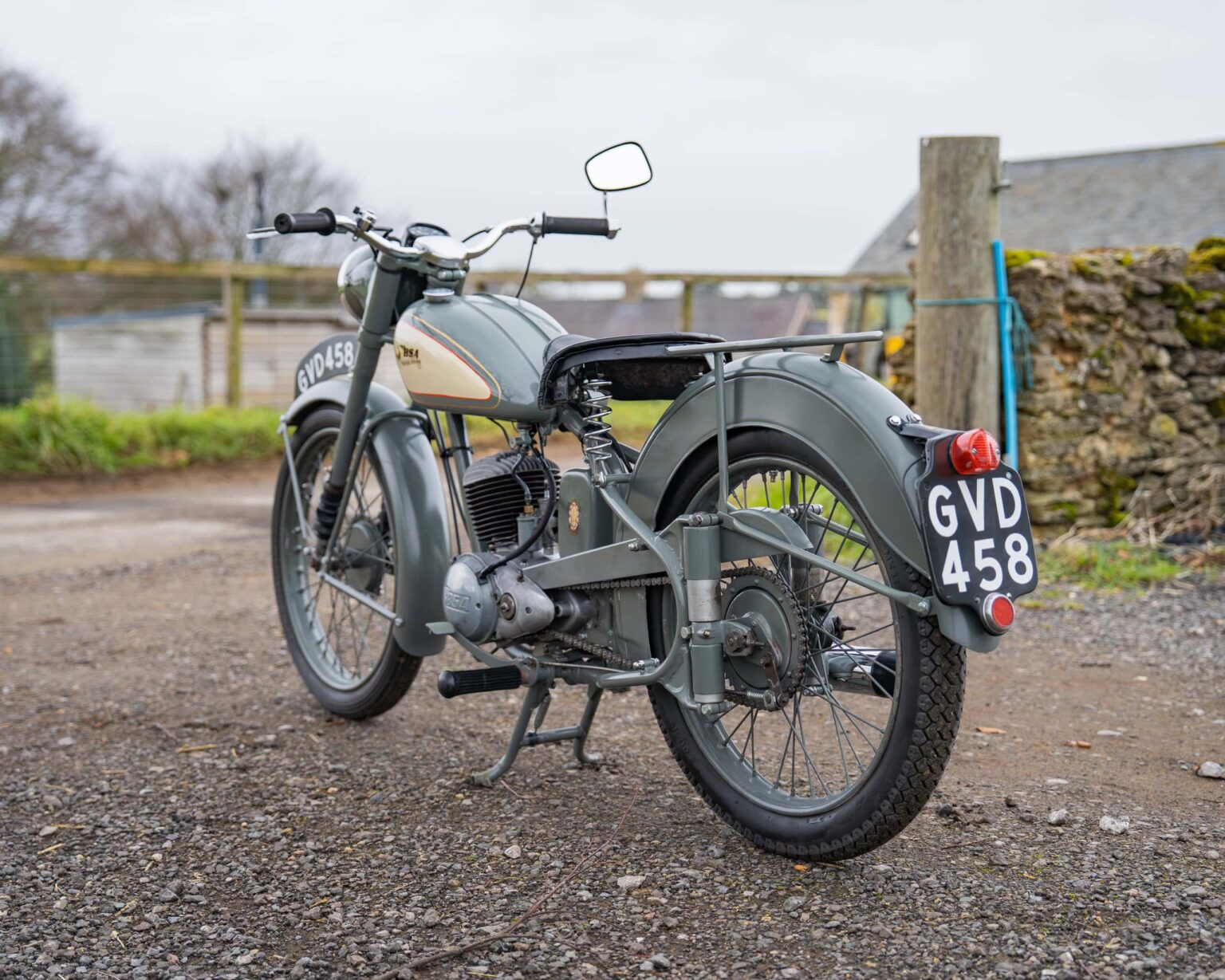 Vintage motorcycle with a grey and cream finish, parked outdoors on a gravel surface.