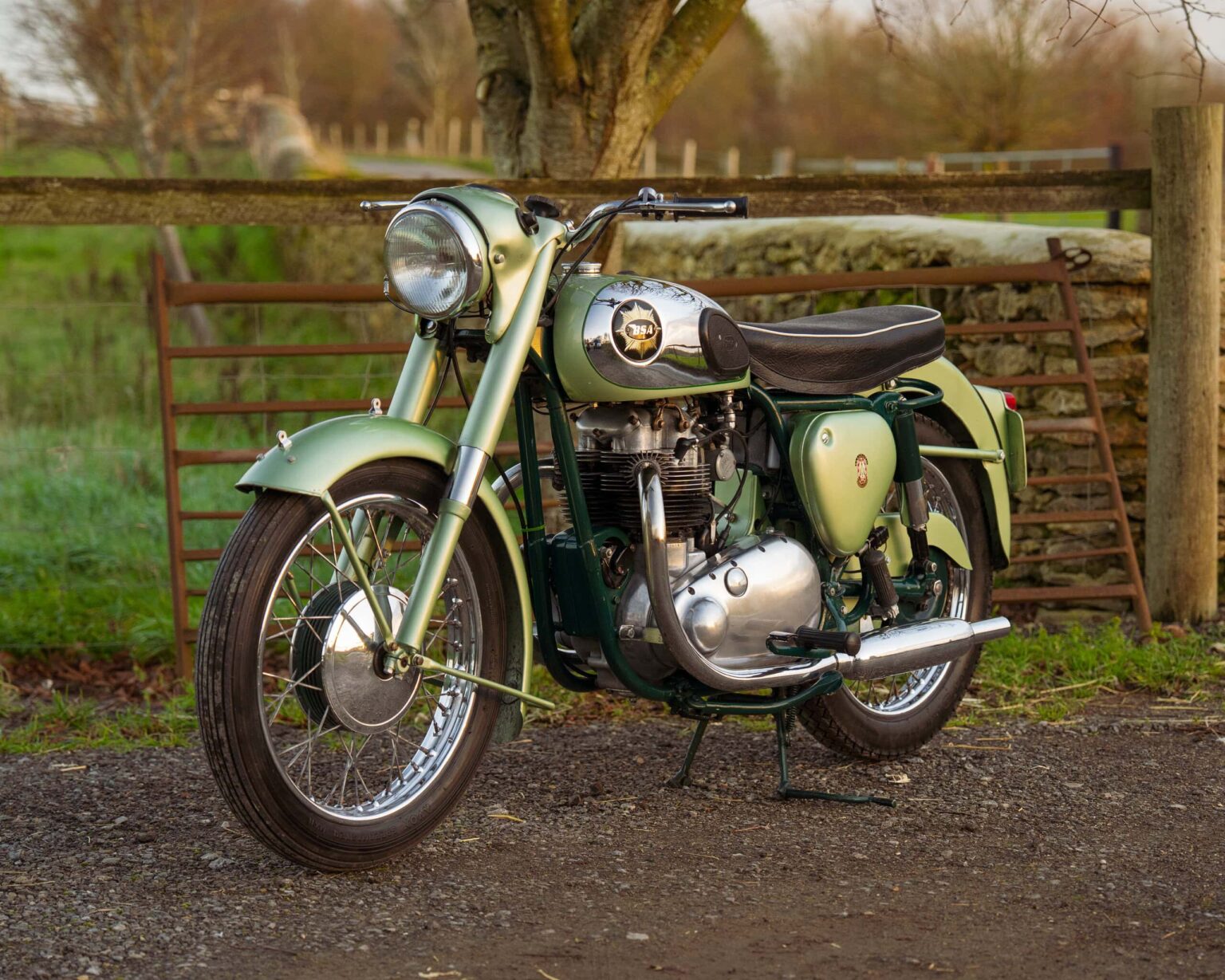 Vintage motorcycle on a country road with a wooden fence.
