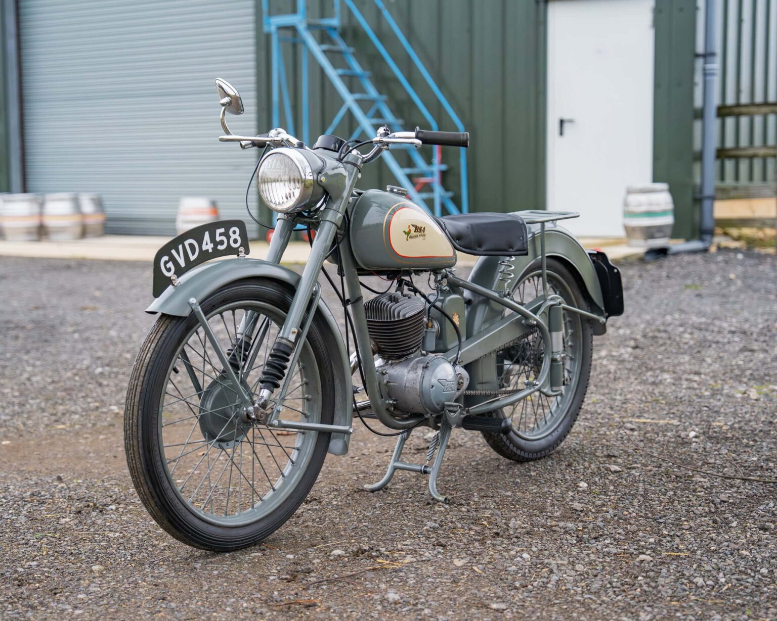 Vintage motorcycle with grey finish and retro design, parked outdoors near industrial buildings.