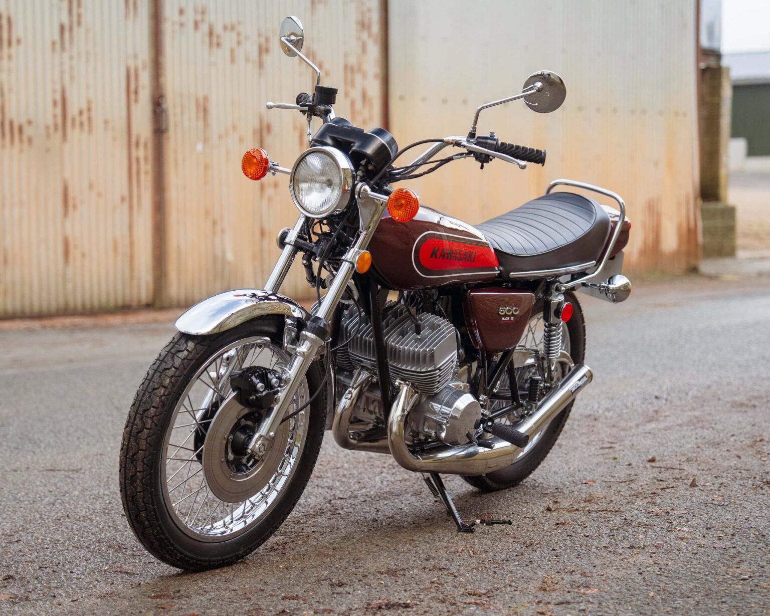 Vintage Kawasaki motorcycle parked on street with rusty wall background.