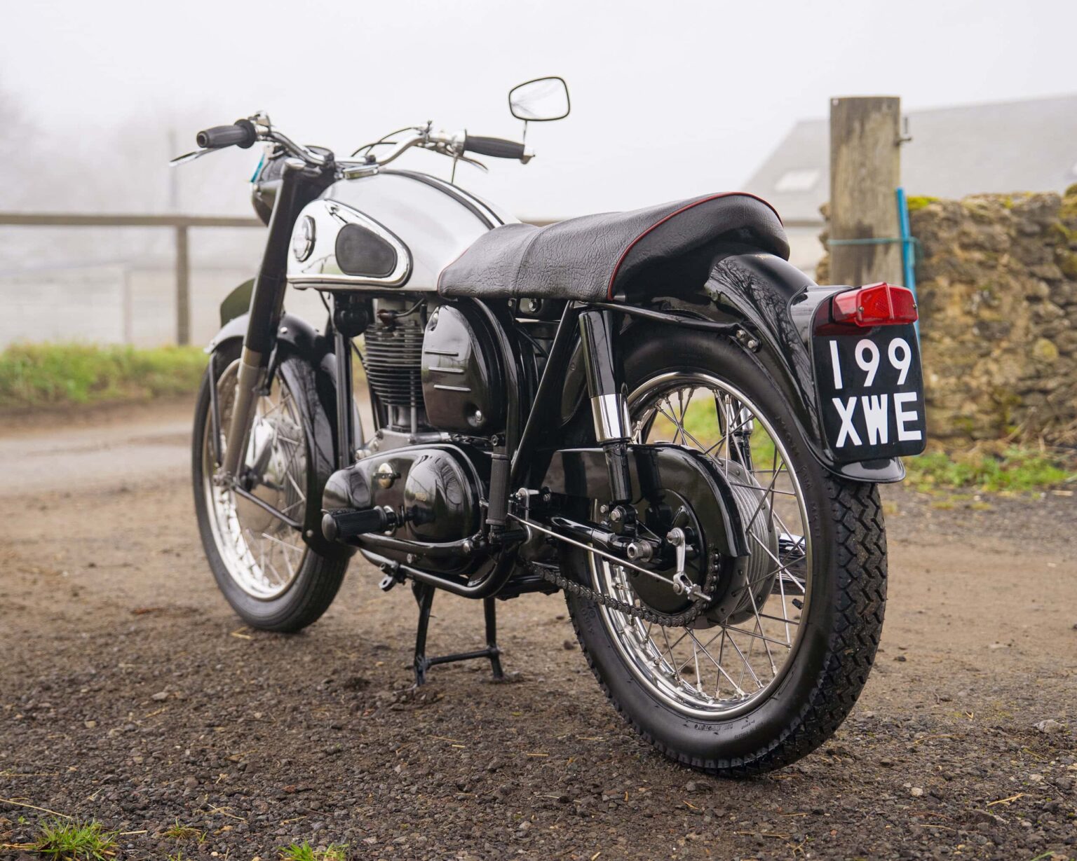 Vintage motorcycle with black and silver finish, parked outdoors on a dirt track.
