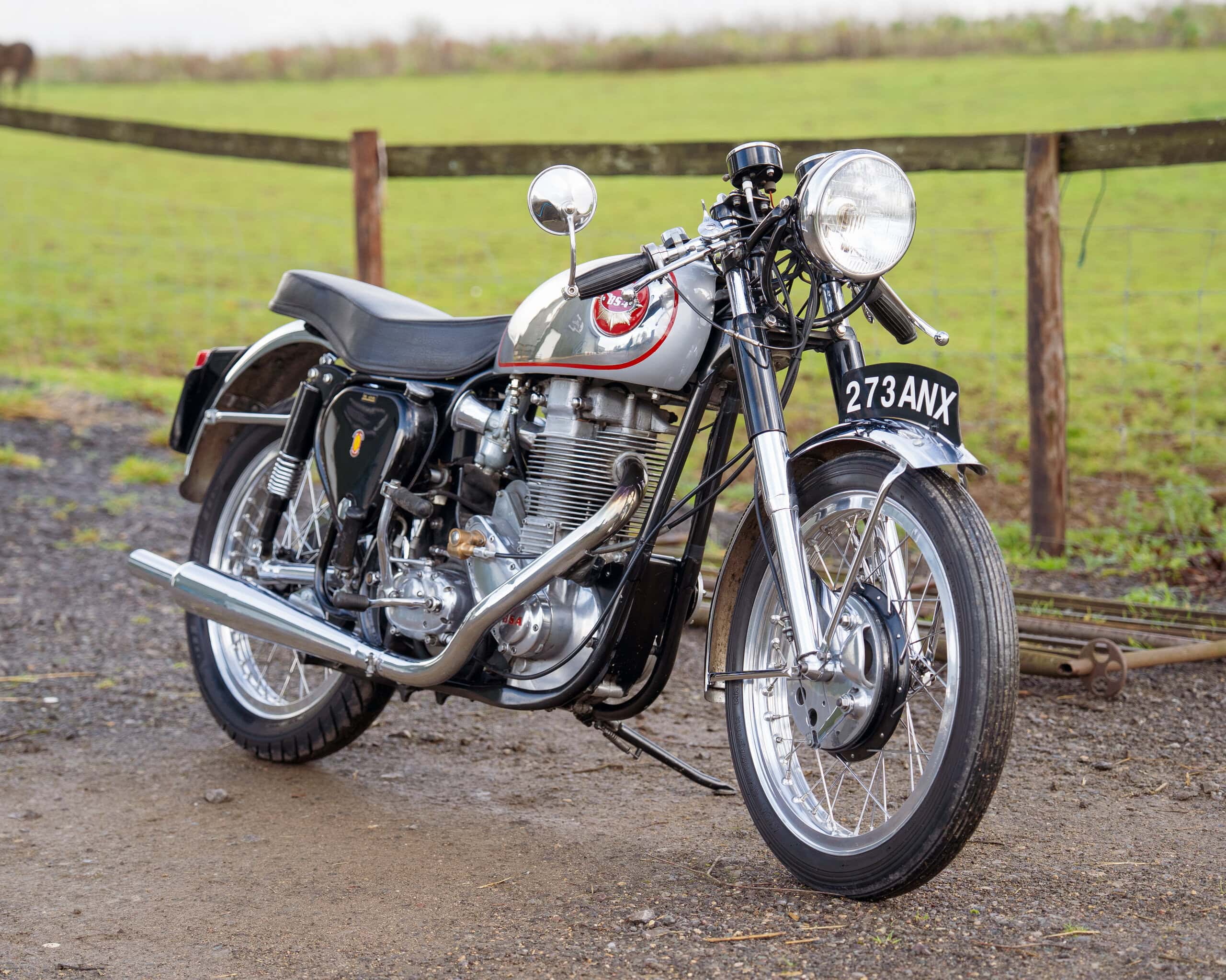 Motorcycle parked outdoors with a rural background and wooden fence.