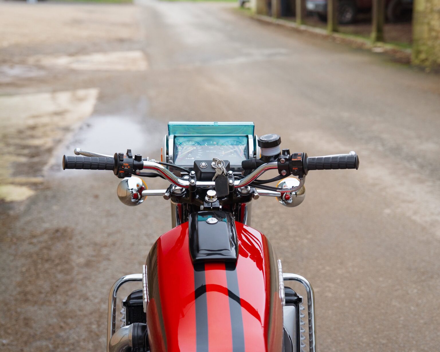 Motorcycle handlebars with dashboard and phone holder on a quiet street.