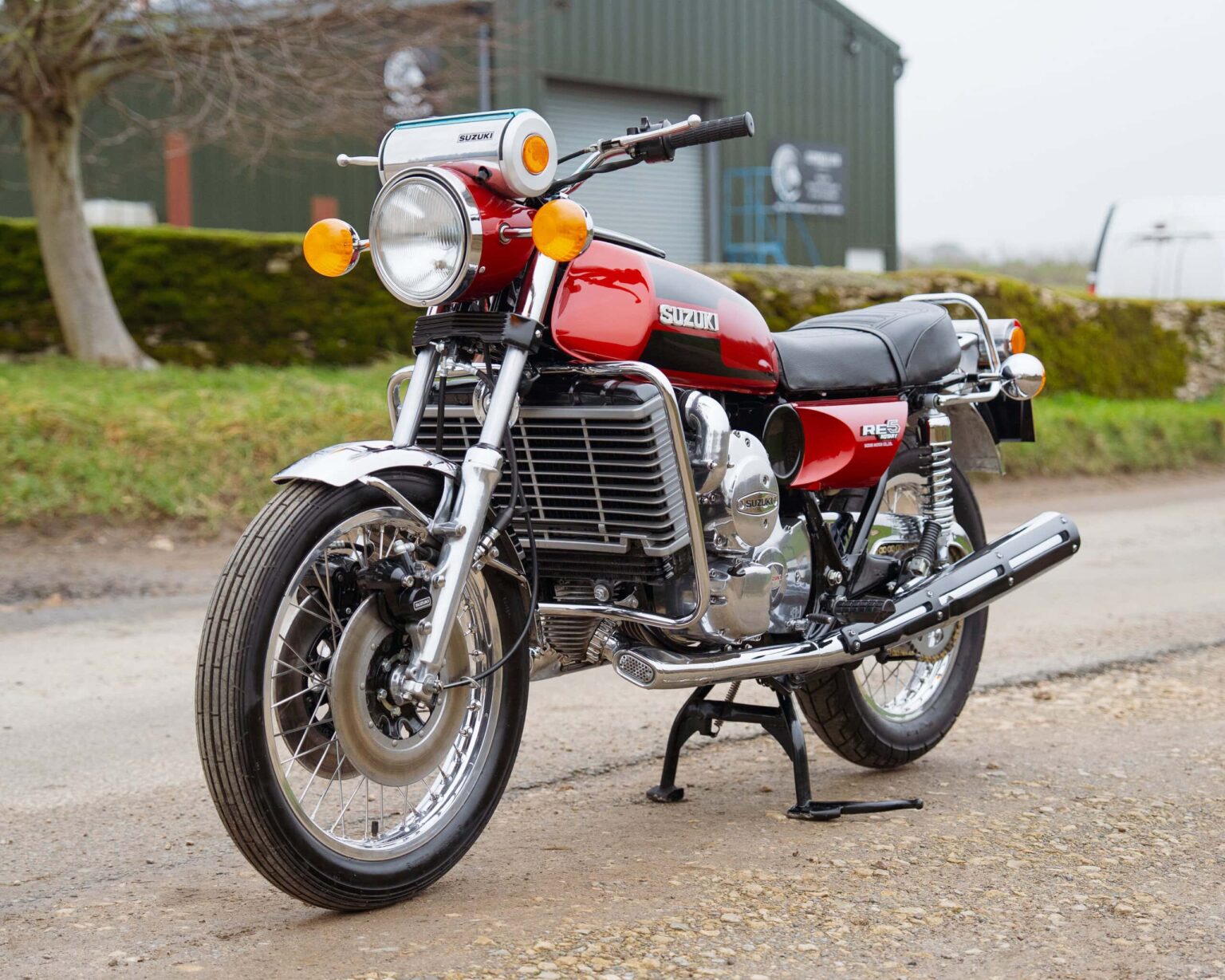 Vintage Suzuki motorcycle parked outdoors with green industrial building in background.