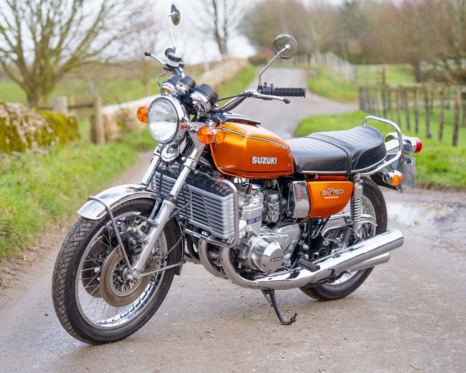 Vintage orange Suzuki motorcycle parked on a country road.