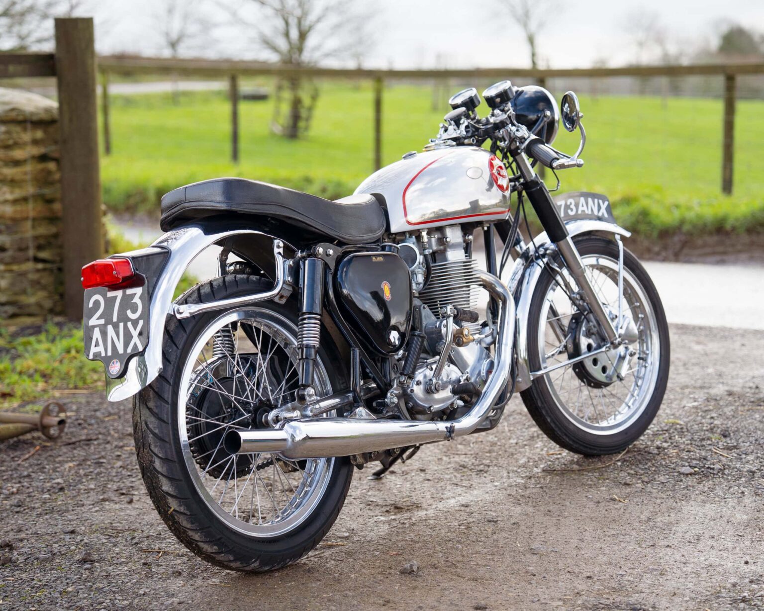 Vintage motorcycle with a silver and black finish, parked outdoors on a gravel surface.