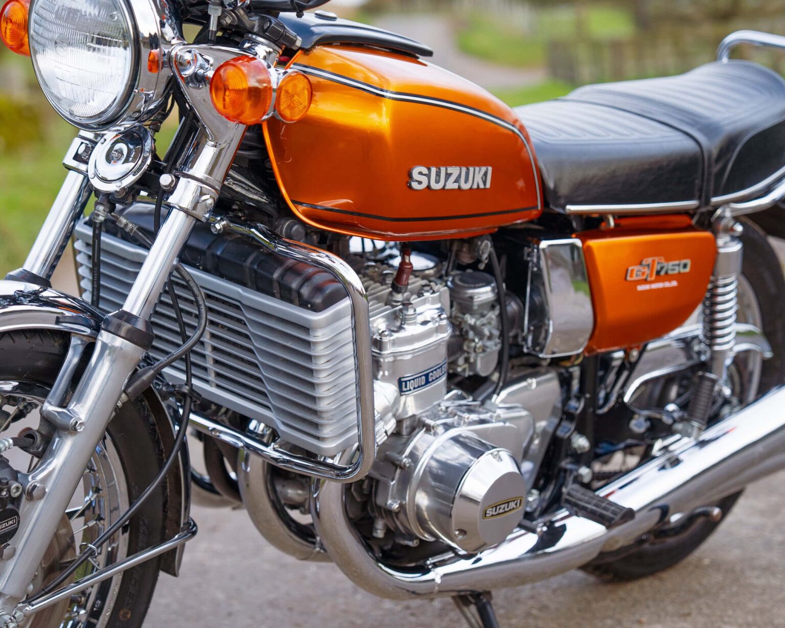 Vintage Suzuki GT750 motorcycle with orange tank and chrome details.