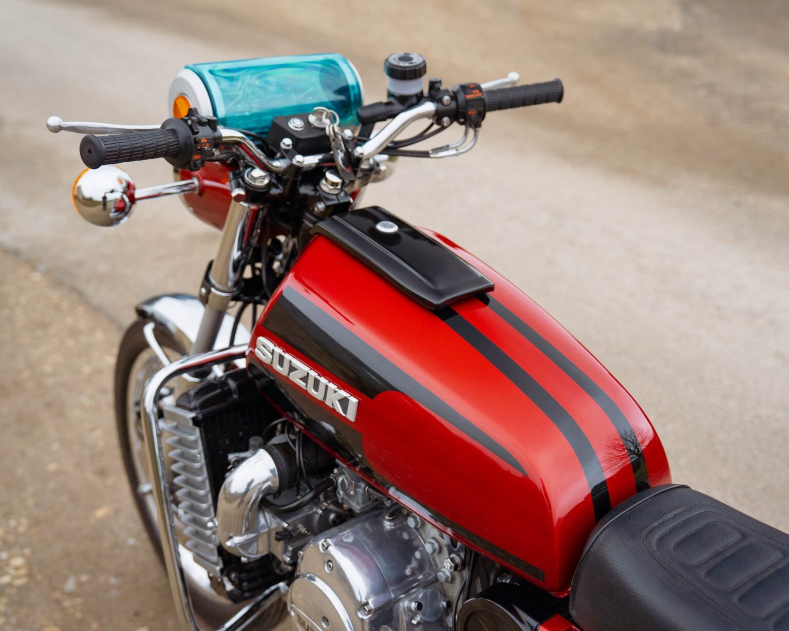 Vintage red Suzuki motorcycle with black racing stripes and handlebar controls.