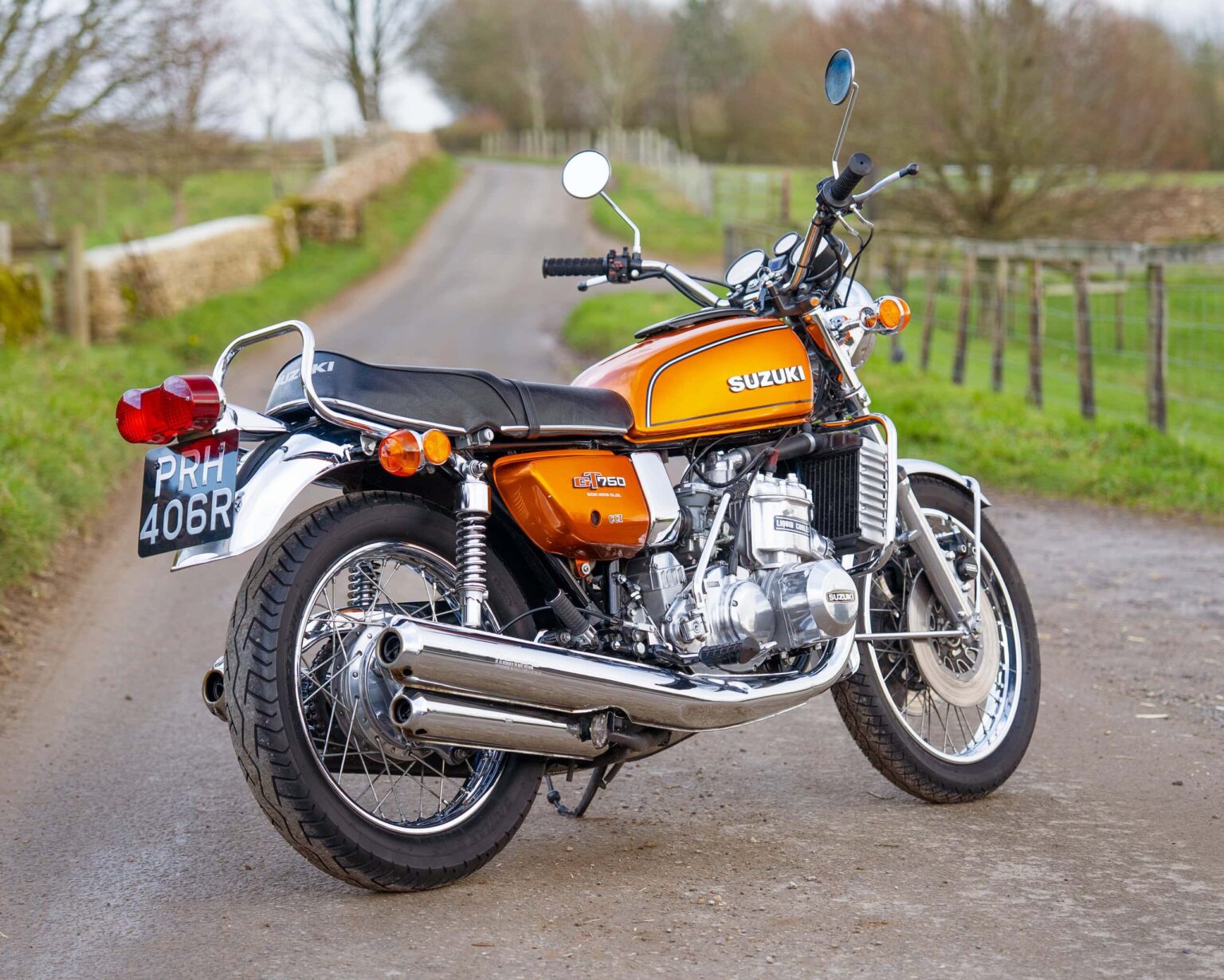 Suzuki vintage motorcycle parked on a rural country road with green fields and trees in the backgrou.